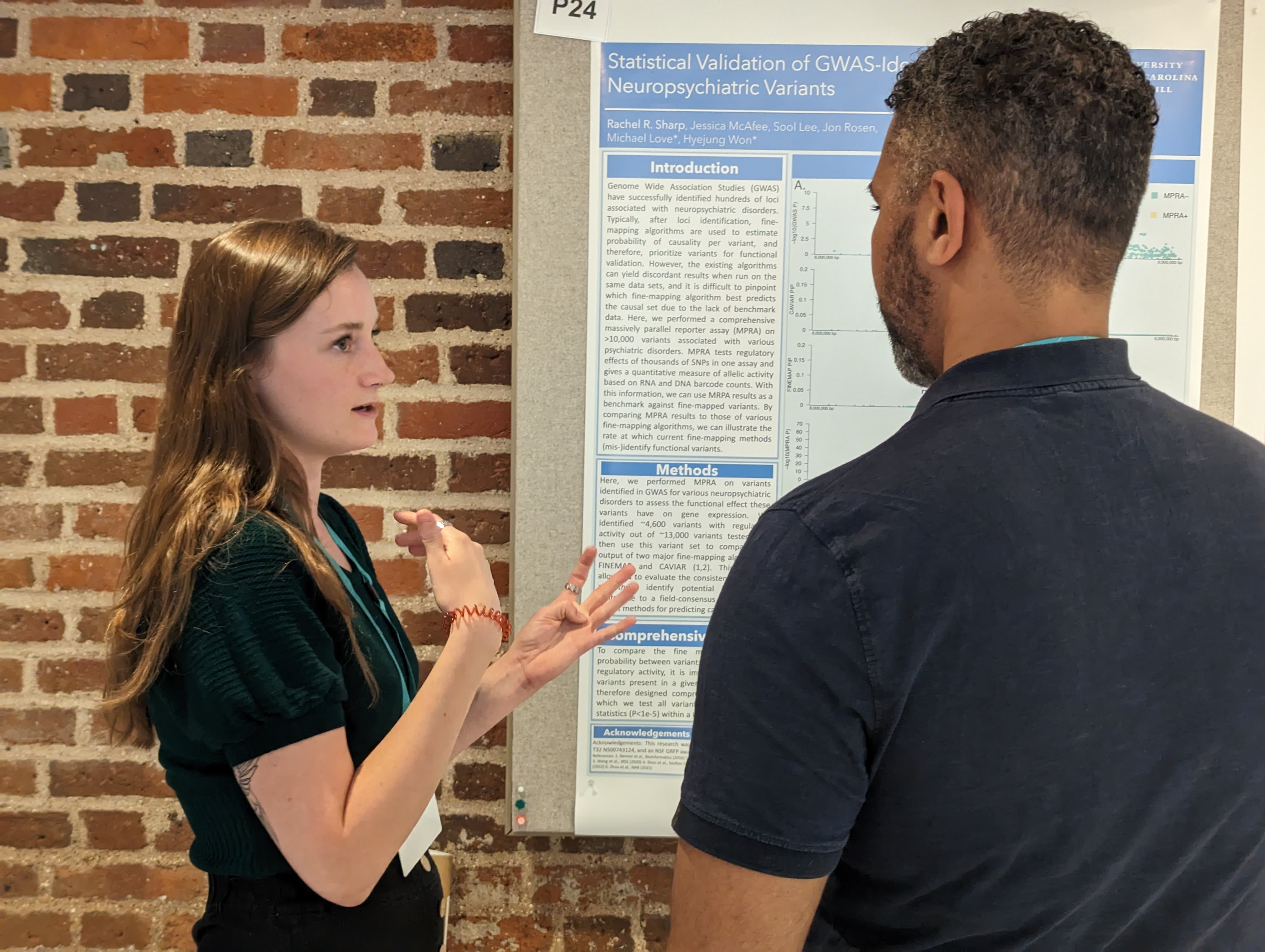 Rachel presenting a research poster. She gestures, mid-sentence, to a man standing his back to you.